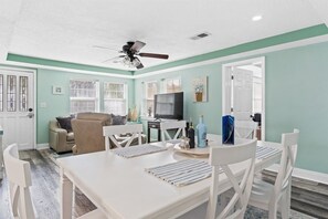 A dining area with a white table and chairs, a ceiling fan, and a television in the background.