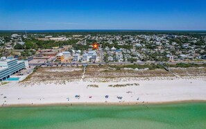 An aerial view of a coastal town with a beach, residential buildings, and a commercial area.