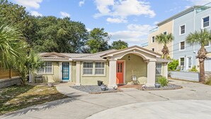A two-story residential building with a front porch, a red door, and a small garden area with palm trees. - Beach Better | Private Beach Access (Panama City Beach)