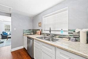 A modern kitchen with a dishwasher, double sink, and a window with blinds.