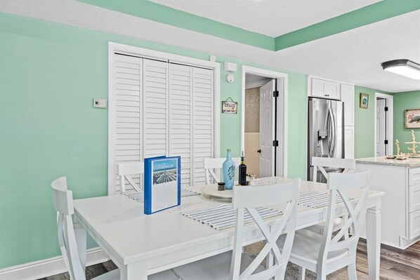 A dining area with a white table and chairs, a blue menu stand, and a refrigerator in the background.