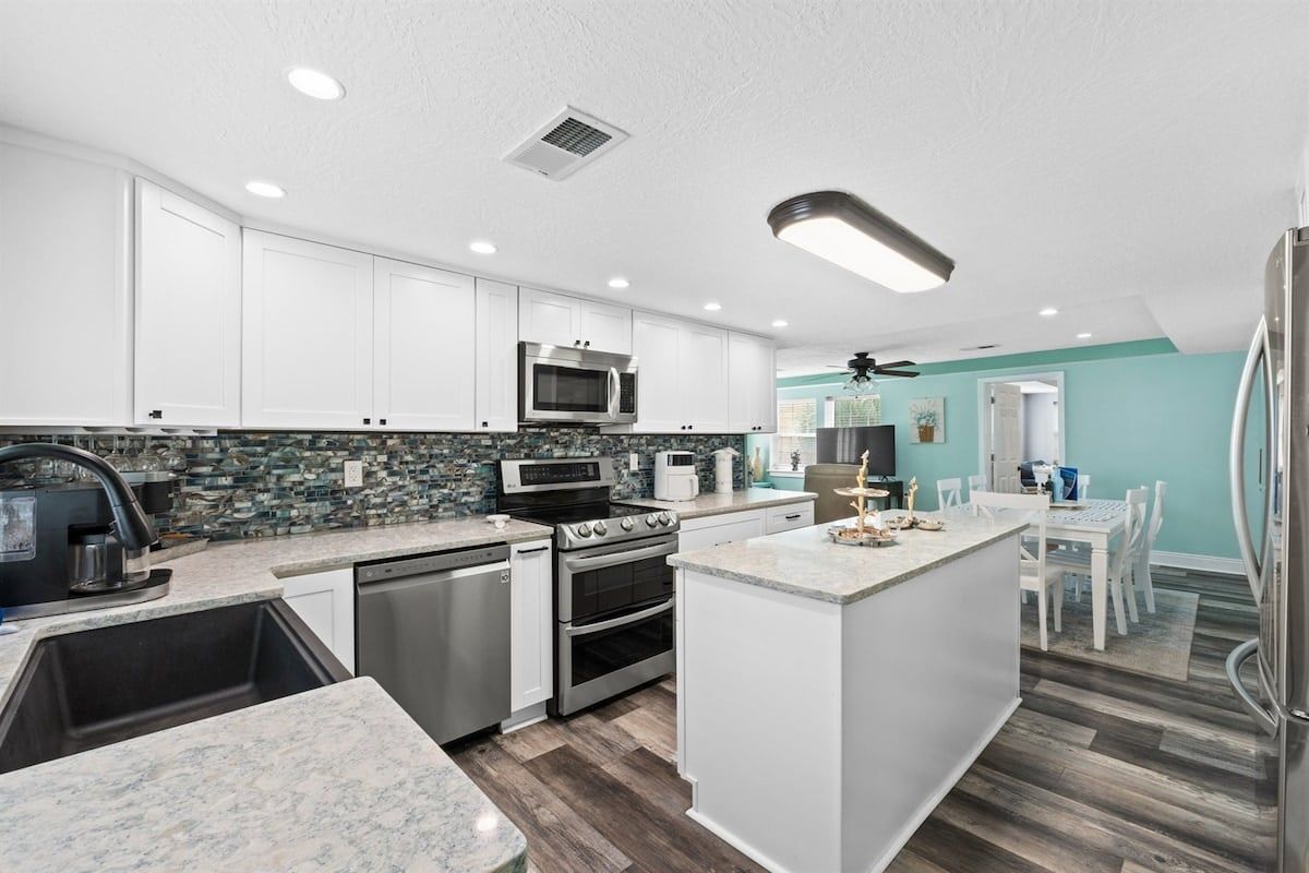 A modern kitchen with white cabinets, a granite countertop, stainless steel appliances, and a teal accent wall.