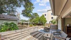 An outdoor patio with wooden deck, seating area, and a view of neighboring buildings. - Beach Better | Private Beach Access (Panama City Beach)