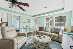 A living room with a ceiling fan, a beige sofa, a round ottoman, and a coffee table. - Beach Better | Private Beach Access (Panama City Beach)