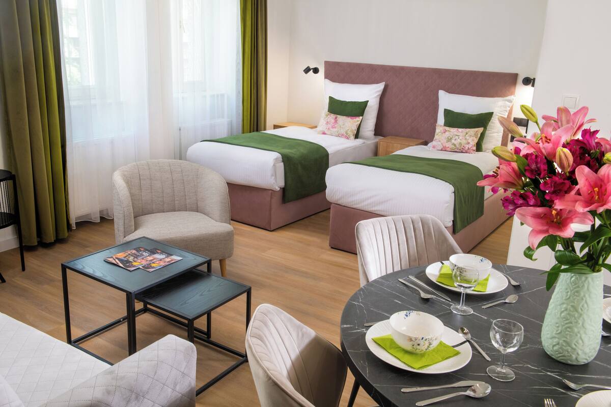 A hotel room with two beds, a dining table set for two, a small armchair, and a coffee table.