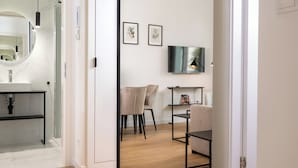 A modern bathroom with a large mirror, a sink, and a shower. There is a seating area with chairs and a table, and a television mounted on the wall. - Rajska Residence (Kraków)