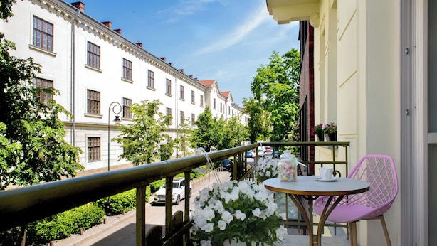 A balcony with a table and chairs, overlooking a street with parked cars and buildings. - Rajska Residence (Kraków)