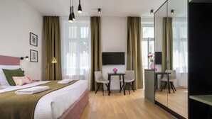 A hotel room with a bed, a desk, chairs, a TV, and a large mirror. - Rajska Residence (Kraków)