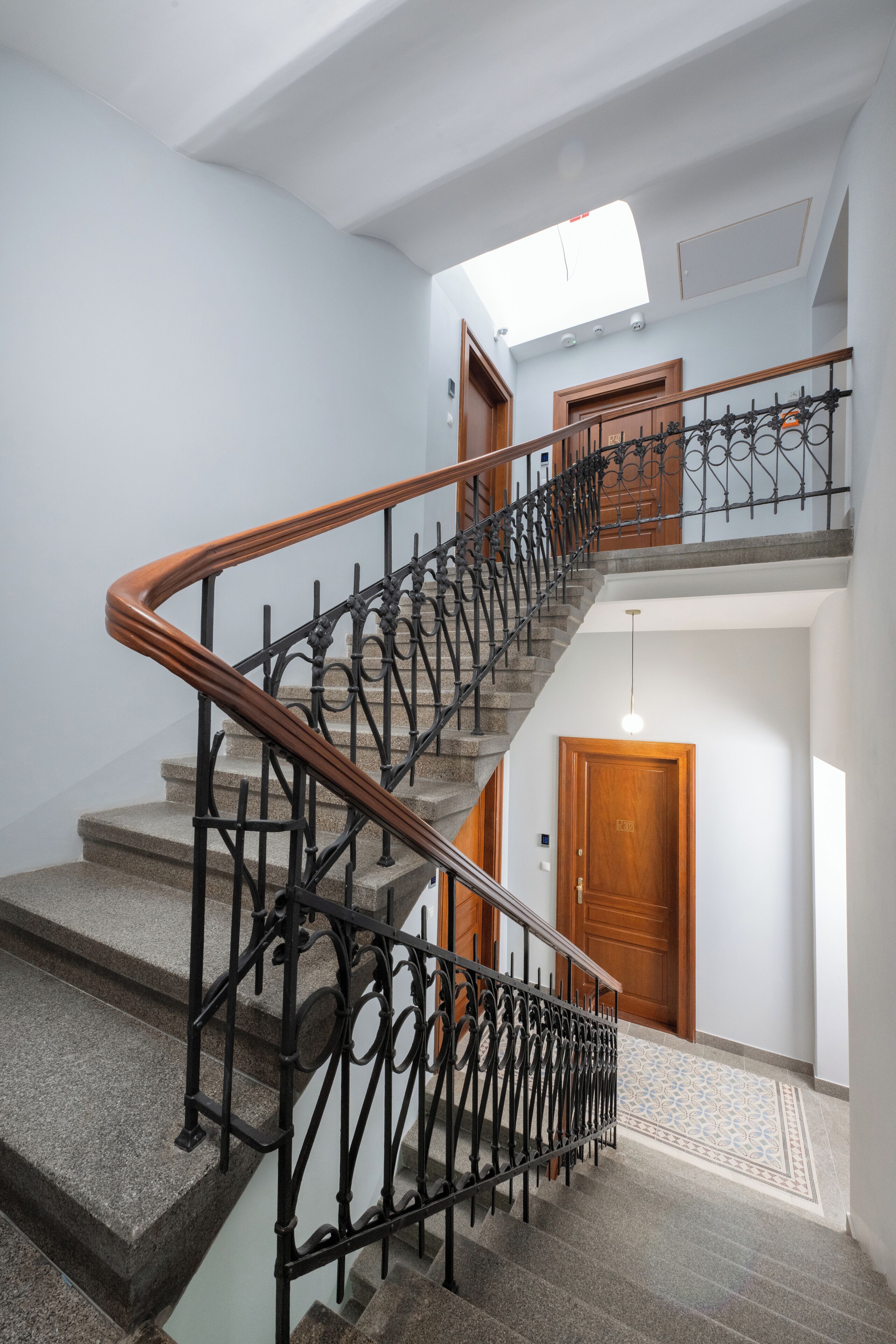 A multi-level staircase with a wooden handrail and black iron balusters, leading to a wooden door at the top.