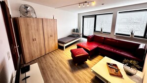 A modern living room with a wooden wardrobe, a red sofa, a small bed, and a white coffee table.