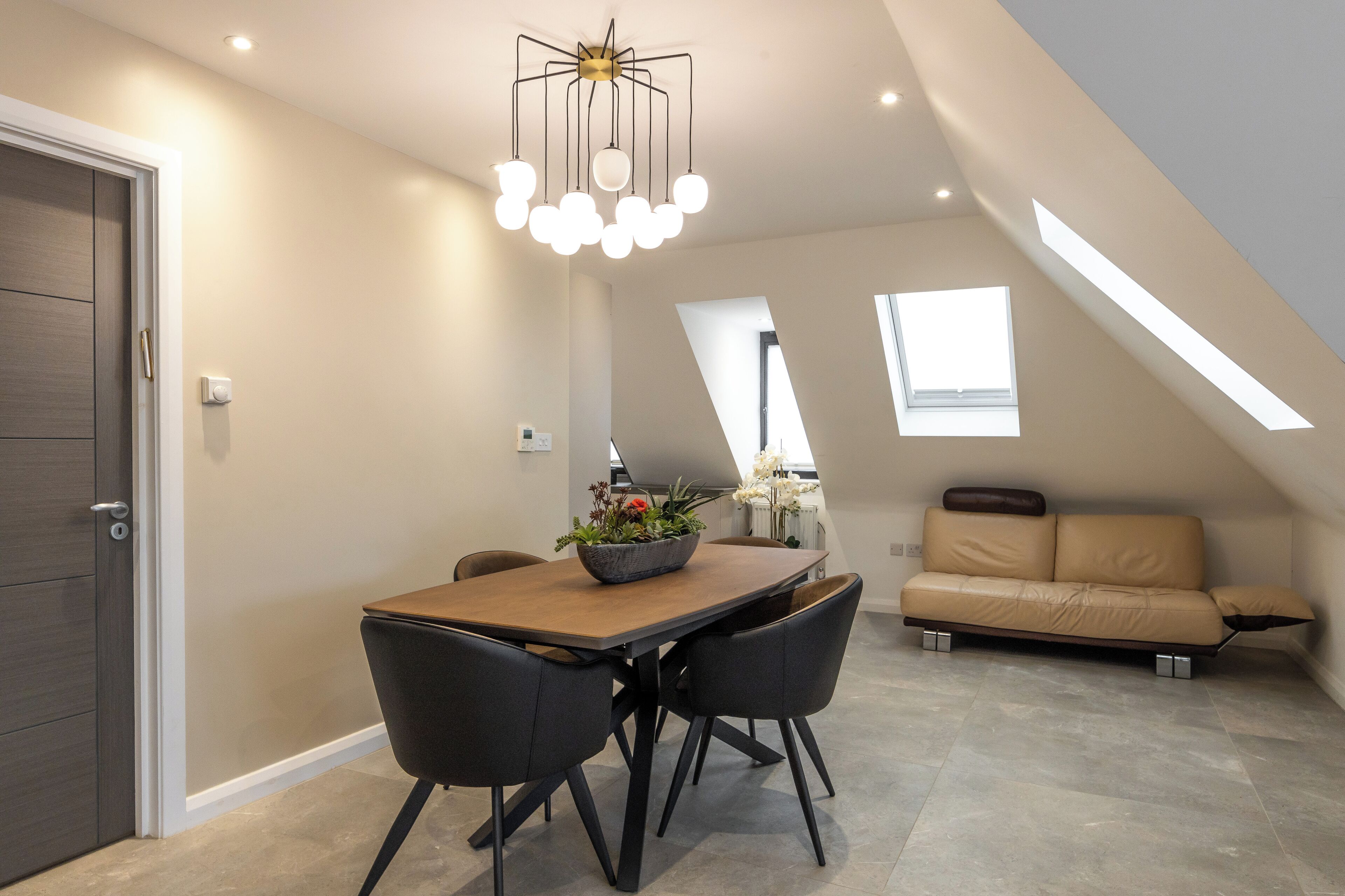 A modern dining area with a wooden table and black chairs, a beige sofa, and a ceiling light fixture.