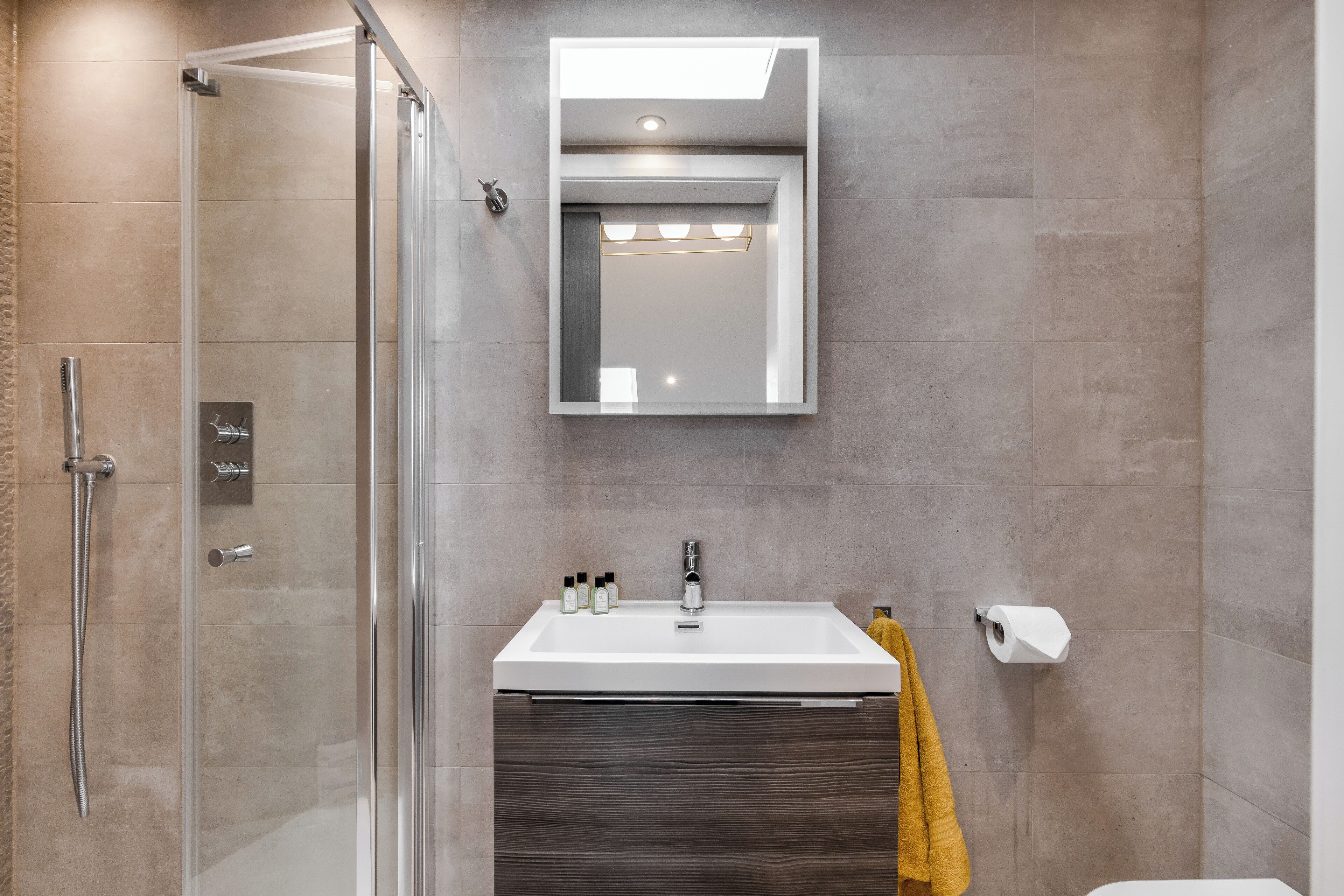 A modern bathroom with a glass-enclosed shower, a white sink with a mirror above, and a towel rack with a yellow towel.