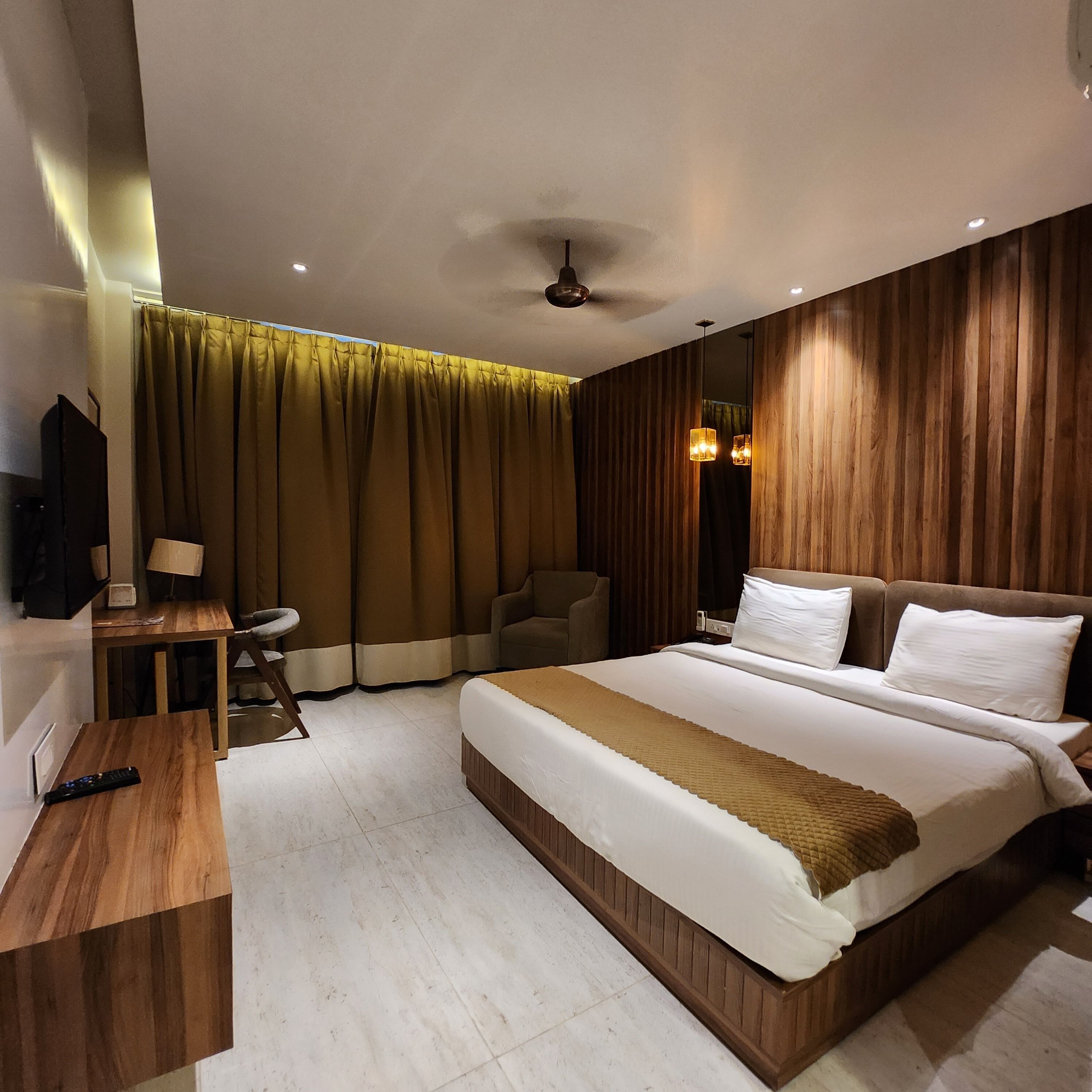 Camera d'albergo moderna con testiera in legno, un letto grande, una scrivania con una lampada e un televisore.
