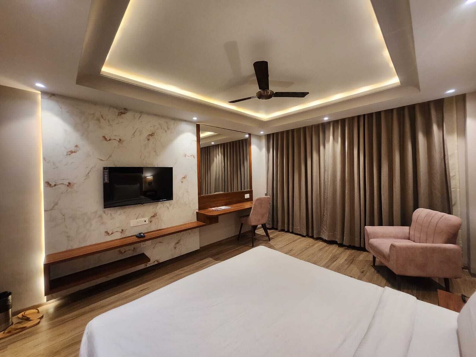 Una habitación de hotel moderna con una cama grande, un escritorio, una silla, un televisor montado en la pared y un ventilador de techo.