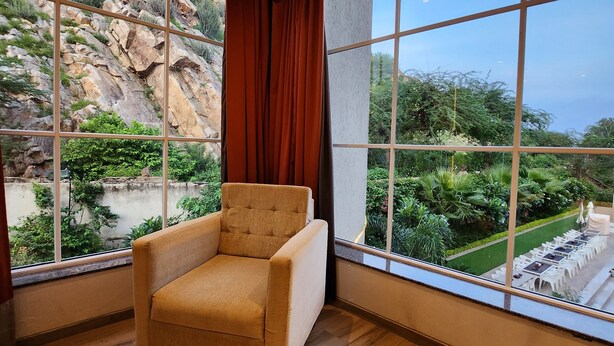 Quarto com uma grande janela que oferece vista para uma paisagem rochosa e vegetação.