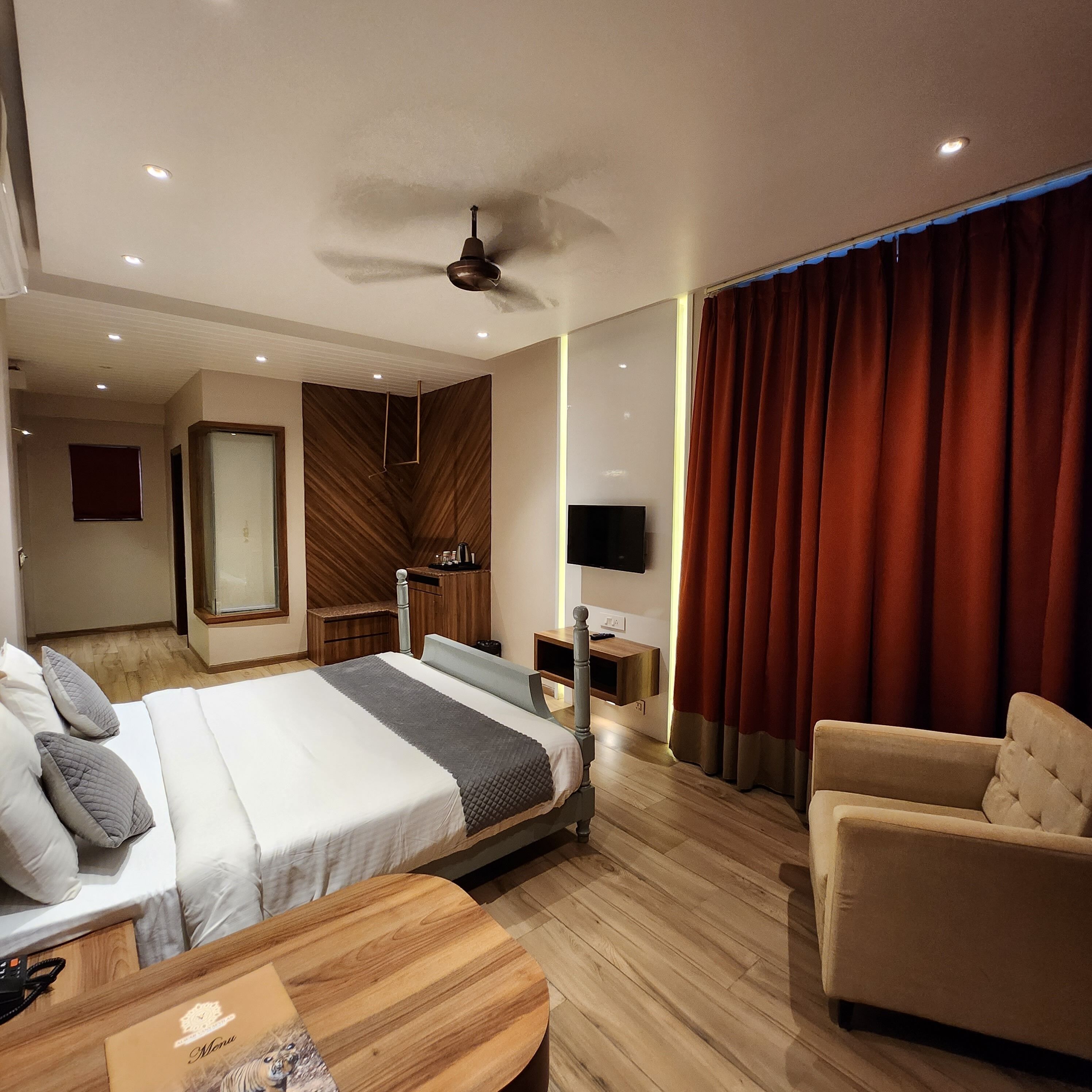A modern hotel room with a large bed, a desk, a chair, a TV, and a ceiling fan.