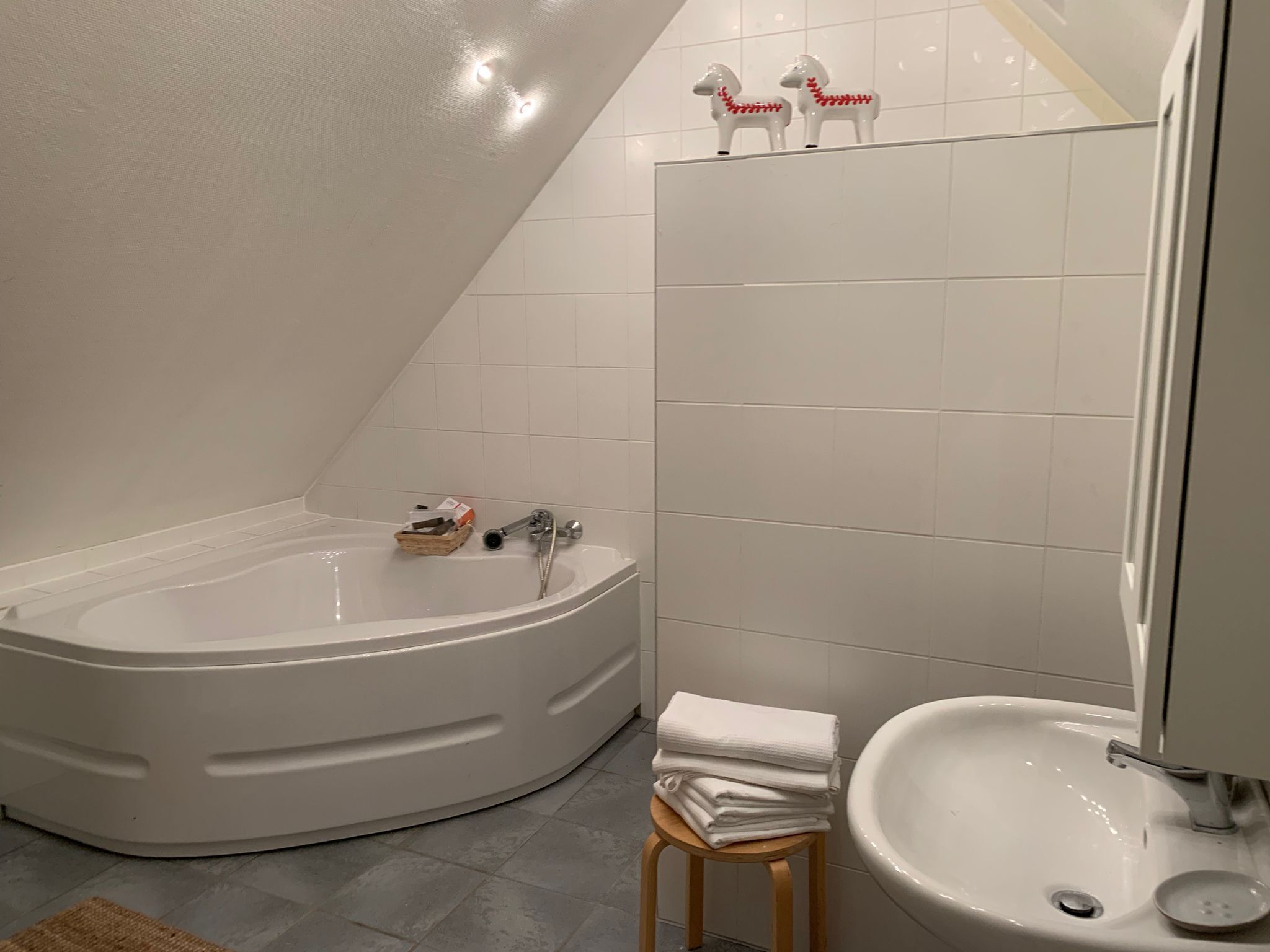 A modern bathroom with a freestanding bathtub, a sink, and a small stool.