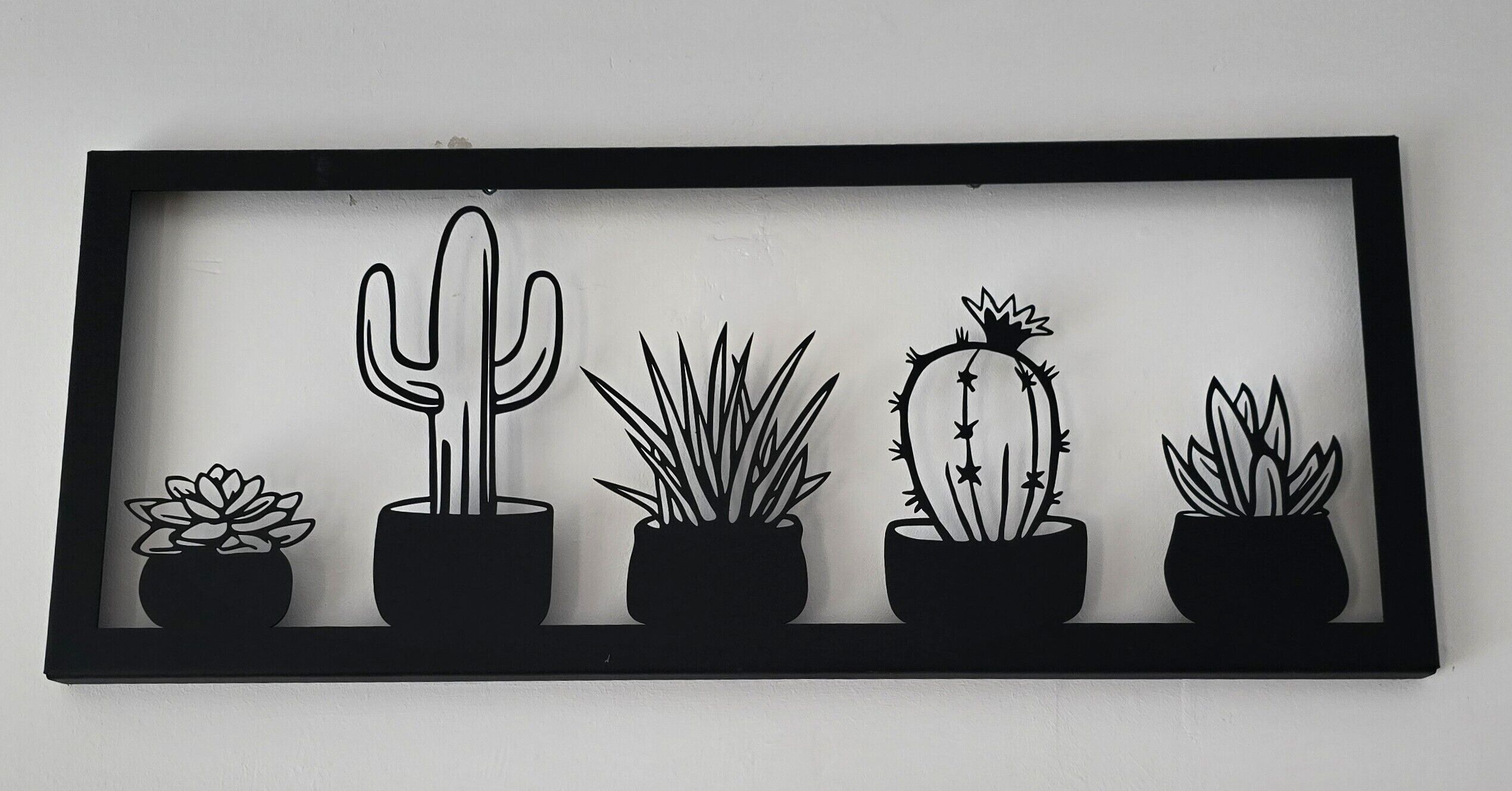Wandkunst mit schwarzen Rahmen, zeigt Silhouetten von fünf verschiedenen Kakteen in Töpfen.