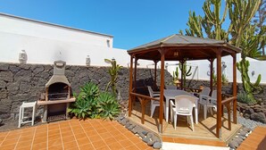 Un patio al aire libre con un pabellón de madera, una pared de piedra y cactus.
