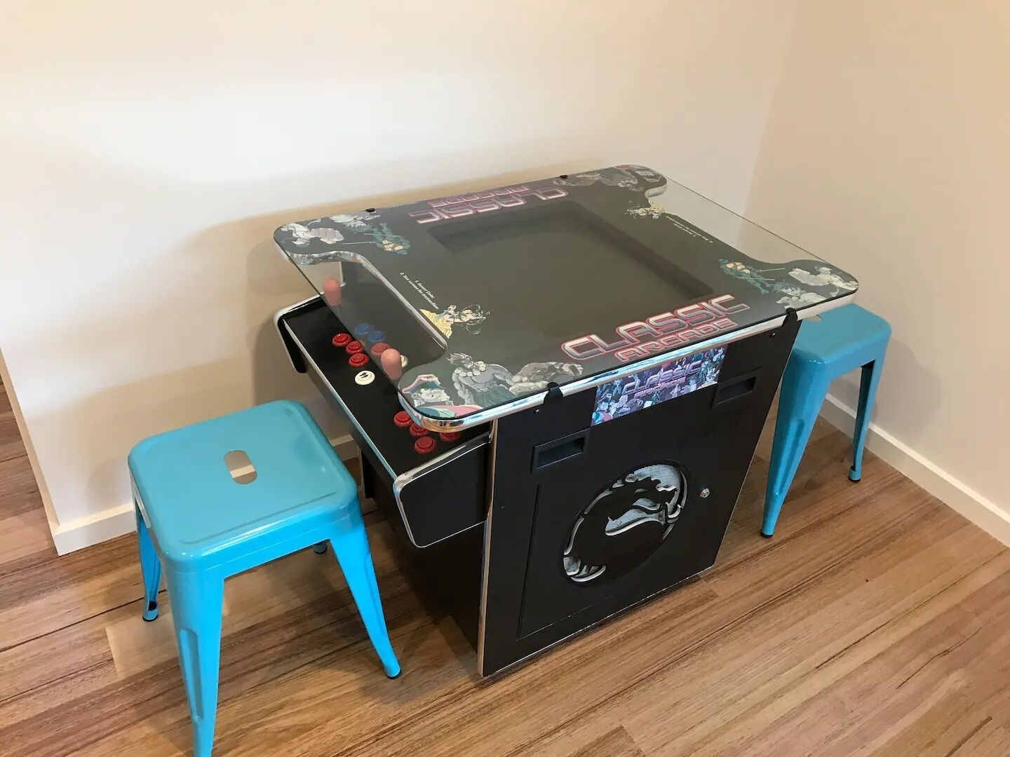A classic arcade machine with a glass top and two blue stools.