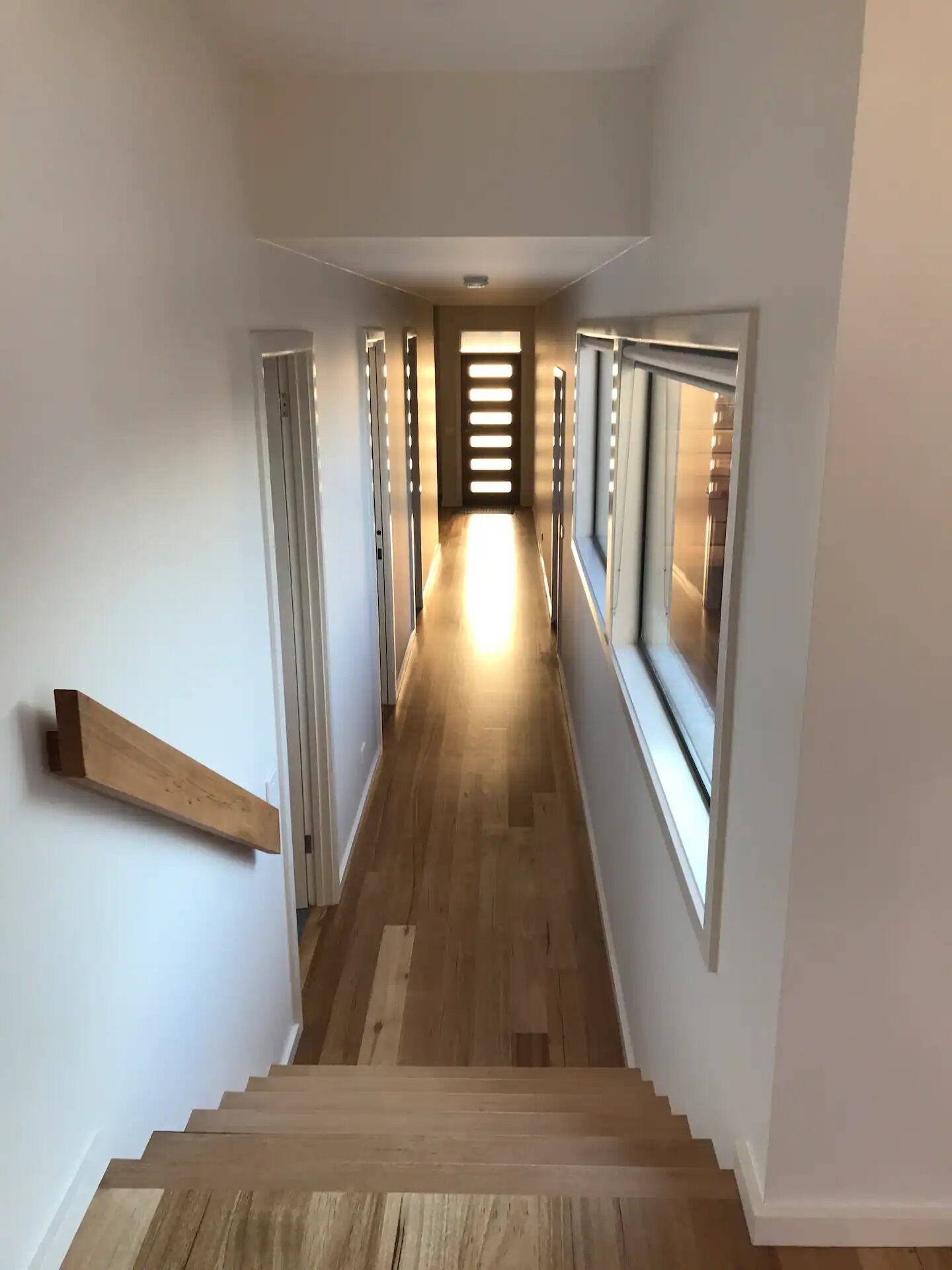 A hallway with wooden flooring, white walls, and a staircase leading to a landing.