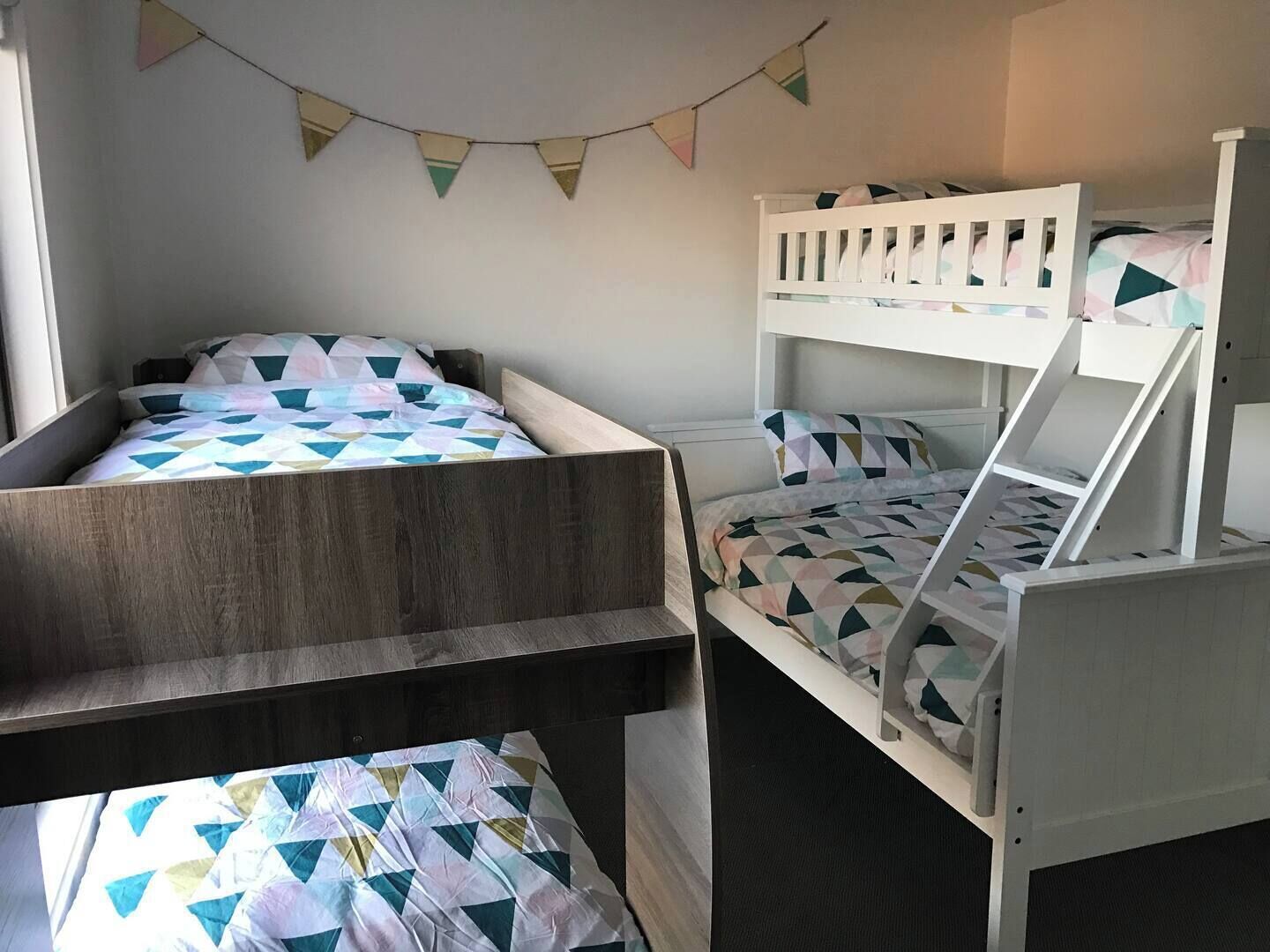 A room with two bunk beds, one with a wooden frame and the other with a white frame. There is a string of triangular flags hanging on the wall.