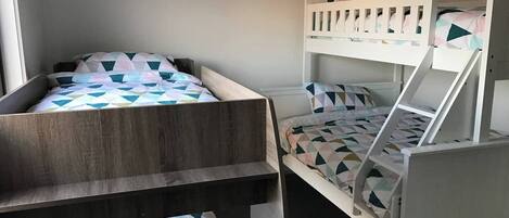 A room with two bunk beds, one with a wooden frame and the other with a white frame. There is a string of triangular flags hanging on the wall.