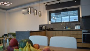 Eine moderne Küche mit einem großen Fenster, einer Obstschale auf dem Tisch und einem Essbereich mit weißen Stühlen.
