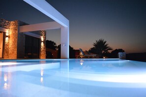 Uma área de piscina moderna ao ar livre, com uma parede de pedra e uma estrutura branca.