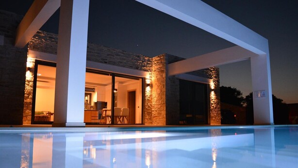 Ein modernes Haus mit Schwimmbad, Steinmauern und großen Glasfenstern, die in einen Innenbereich mit Essbereich führen.