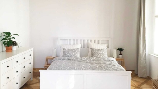 A bedroom with a white bed, a nightstand, a dresser, and a hanging light fixture.