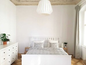 Et soveværelse med en hvid seng, et natbord, en kommode og en hængende lampe.