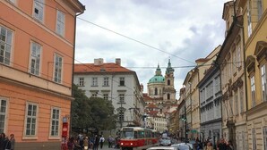 A cobblestone street with historic buildings, a tram, and pedestrians.