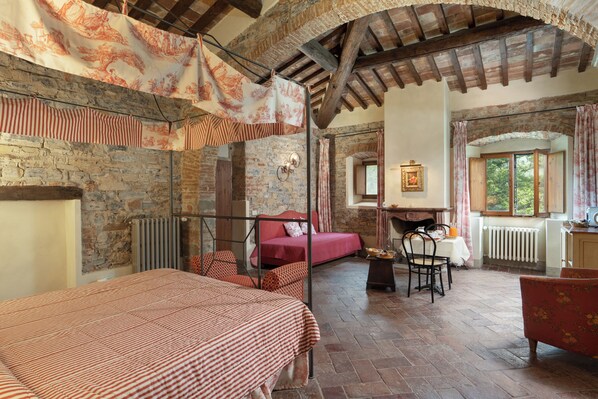 A rustic room with a bed, a red sofa, a dining table, and a window with curtains.