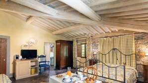 A cozy room with a bed, a table set with breakfast, a television, and a stone wall. - Locanda Di Alberi (Borgo San Lorenzo)