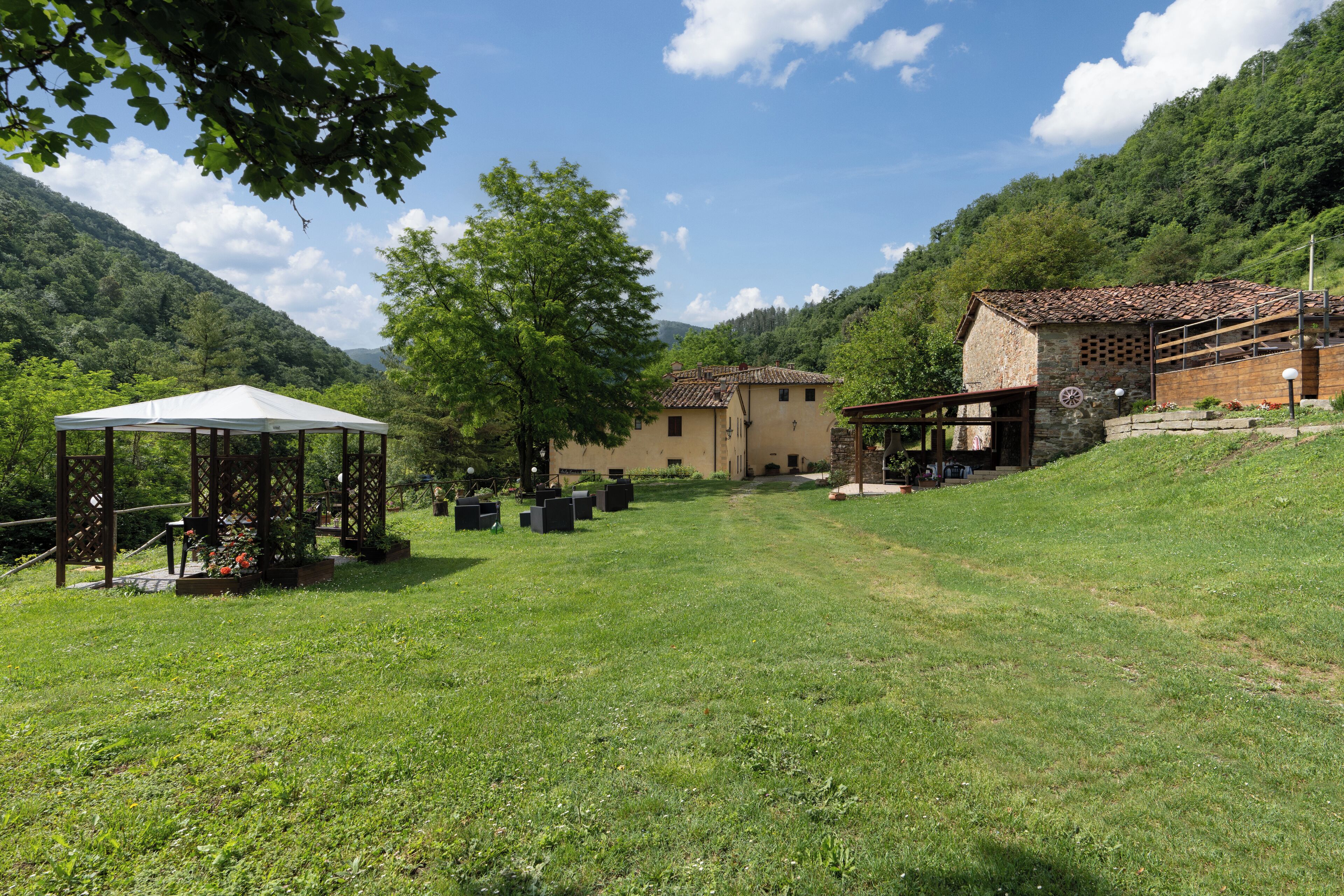 A rural setting with a gazebo, stone buildings, and a grassy area.