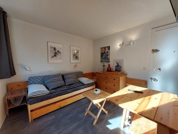 A compact room with a sofa bed, a wooden table, a dresser, and a door.