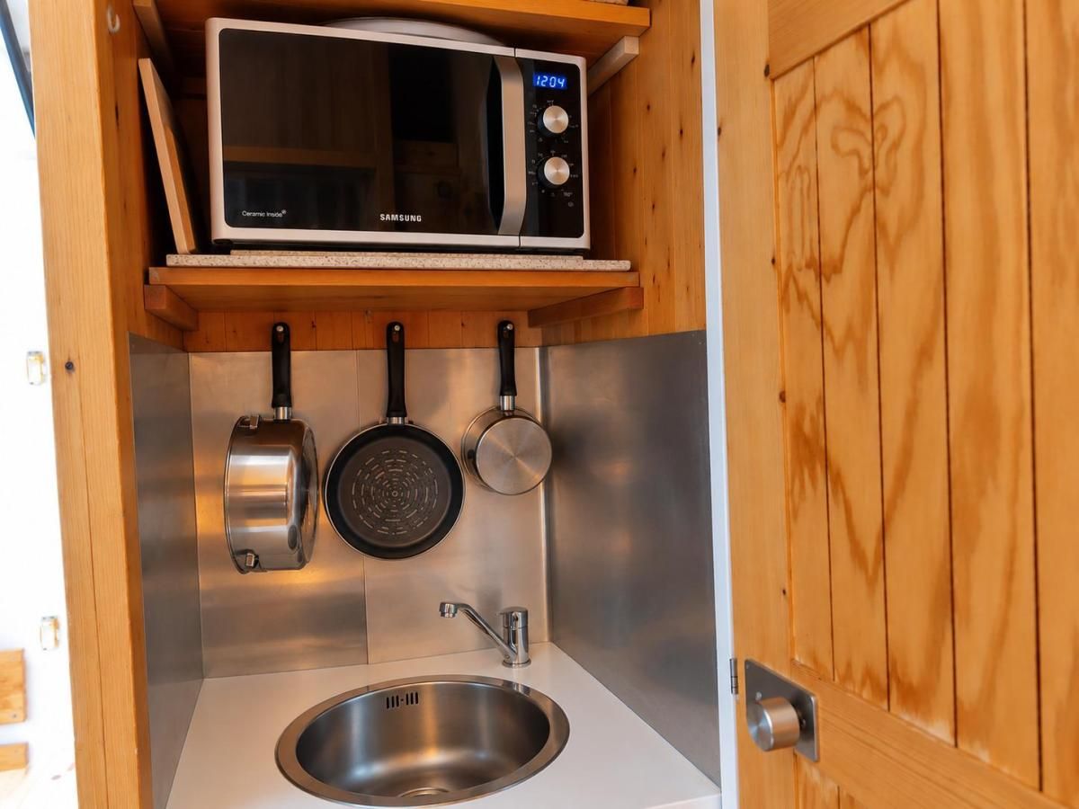 A compact kitchen with a microwave, a sink, and hanging cookware.