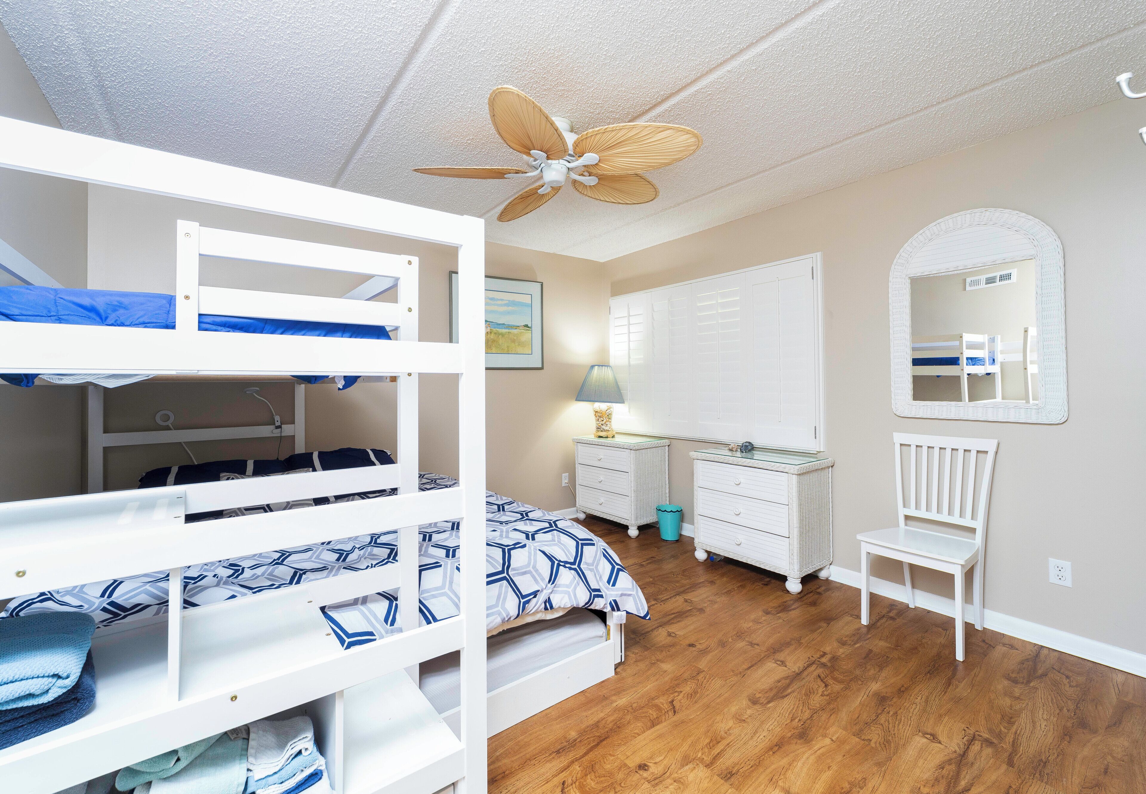 Une chambre avec un lit superposé, un ventilateur de plafond, un bureau, une chaise et un miroir.