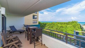 Ein Balkon mit Korbmöbeln, einem Tisch und Stühlen, mit Blick auf eine üppige grüne Landschaft und das Meer.