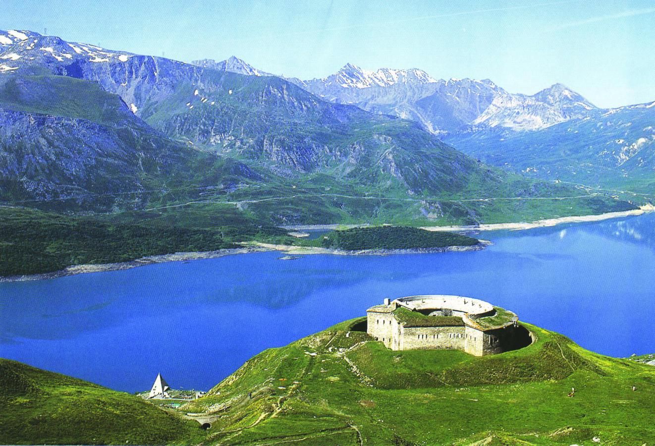 A castle on a hill overlooking a lake with mountains in the background.