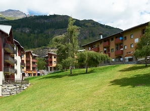 A hotel with multiple balconies, a grassy courtyard, and a mountainous backdrop.