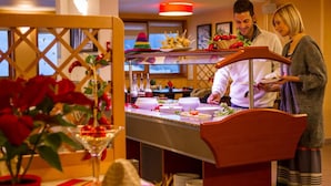 A hotel dining area with a buffet setup, including a variety of dishes and a bartender.