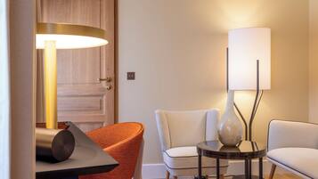 A room with a wooden door, a table with a lamp, two chairs, and a patterned carpet.