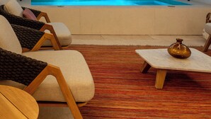 Ein moderner Wellnessraum mit einer großen Whirlwanne, bequemen Sitzmöglichkeiten und einer dekorativen Vase auf einem Tisch.
