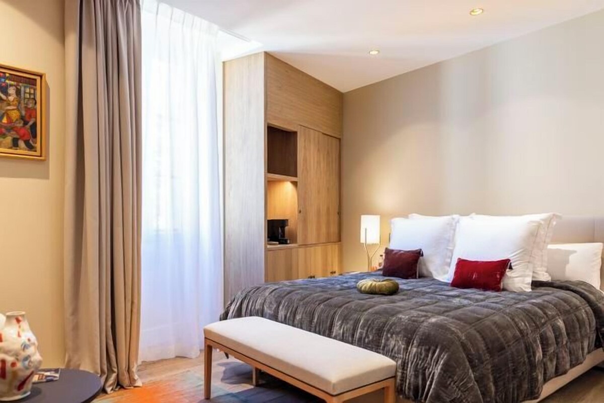 Une chambre d’hôtel moderne avec un grand lit, un banc, une armoire et un tableau au mur.