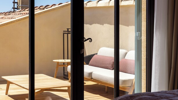 Ein Balkon mit einem Holztisch und Stühlen, einer Couch mit Kissen und Blick auf die Außenansicht des Gebäudes.