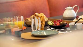 Une table mise pour le petit-déjeuner, avec un bol de fruits, une théière et une tasse de café.