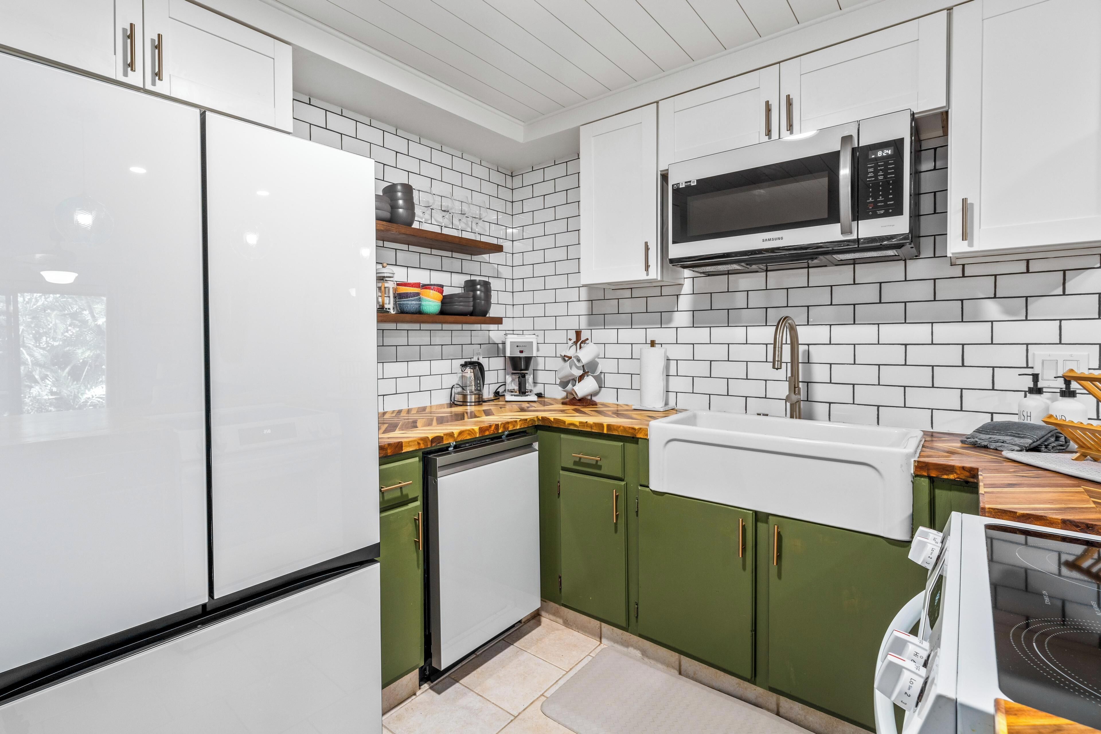 Una cocina con armarios blancos, microondas, lavavajillas y encimera de madera.