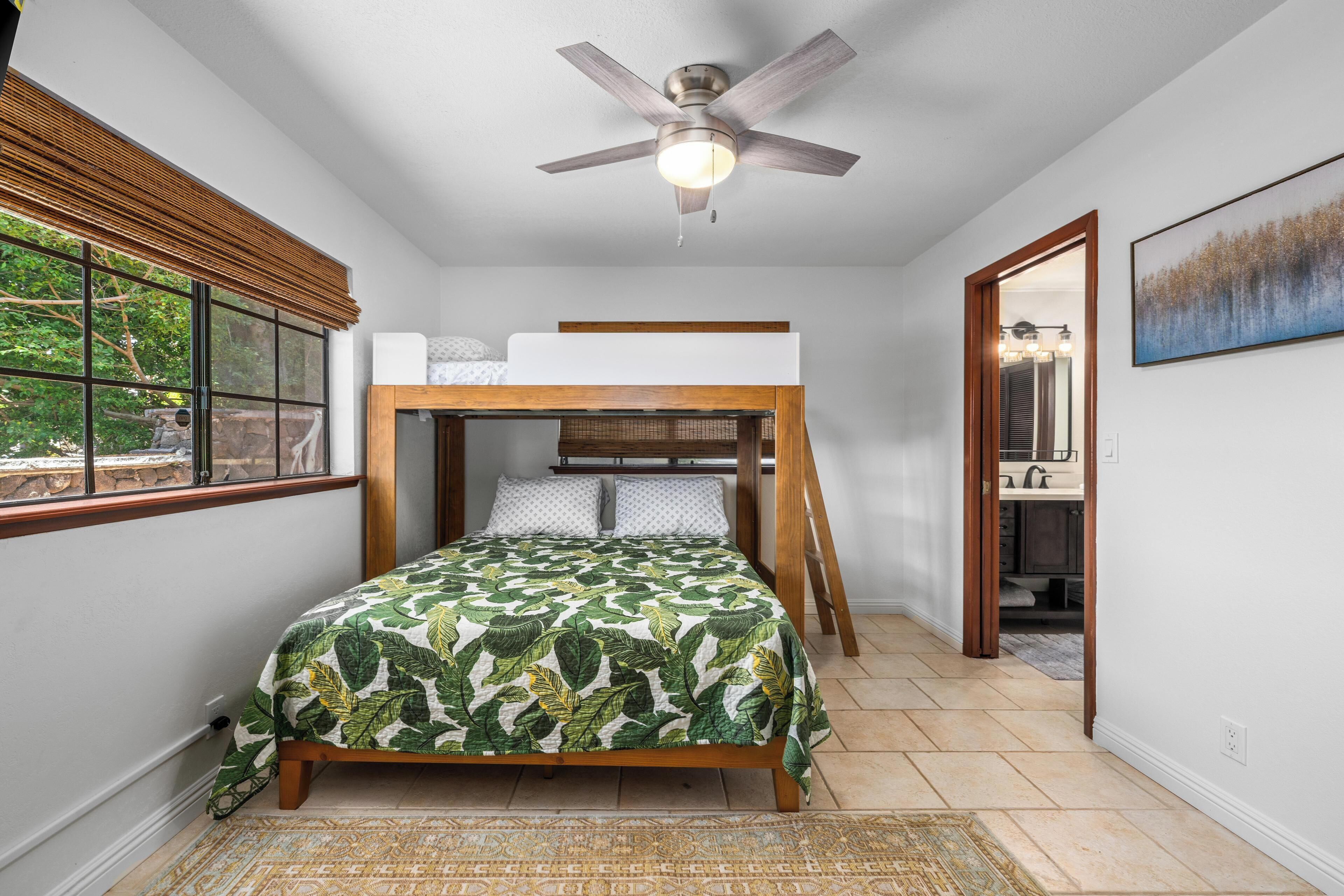 Un dormitorio con literas, ventilador de techo, ventana con persianas y un cuadro en la pared.